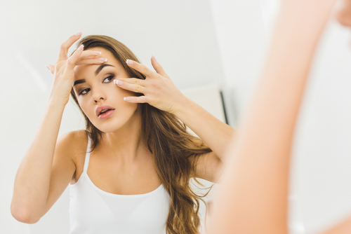 woman checking her face for volume loss in the mirror