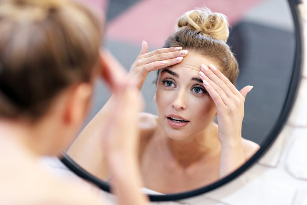 Woman looking at wrinkles and signs of aging in mirror. 